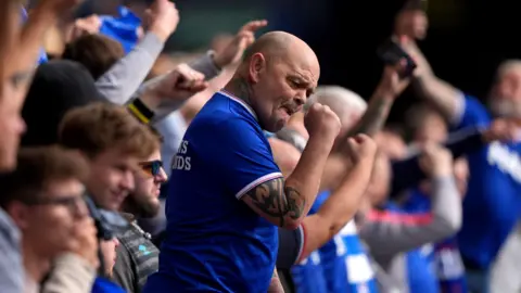 PA Media Ipswich Town fans in the stands before the Sky Bet Championship match at Portman Road, Ipswich. One fan in central focus is lifting his fist in celebration.