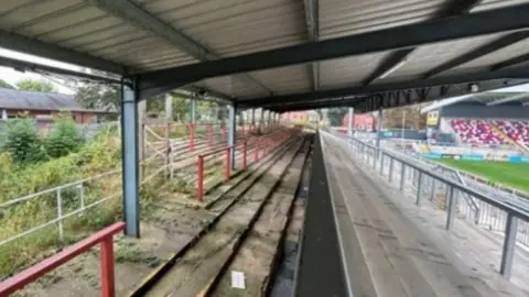 Pegasus Group Inside the North Stand at Wakefield Trinity's rugby league ground with concrete steps to stand on and red railings covered by a roof