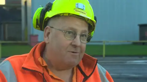 Nigel Kemp, who is wearing a bright yellow hard hat and a bright orange fleece, pictured in his mining days.