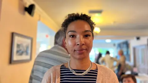 Jazmine is wearing a black and white stripped top and a peach colour jacket. 