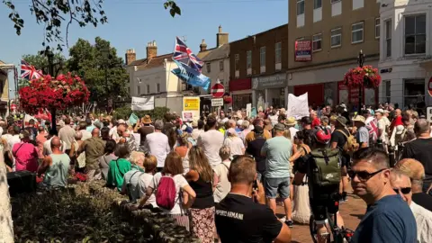 A crowd of people in a high street, with several banners and union flags flying