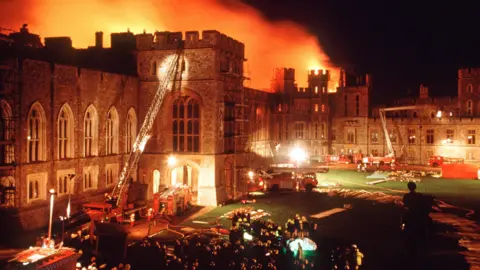 Getty Images A large castle on fire in the distance, with large crowds of firefighter and fire engines in front tackling the blaze