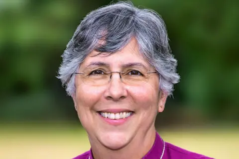 Diocese of Chelmsford Dr Guli Francis-Dehqani's with short hair smiling at the camera. She is wearing a purple top and standing outside.