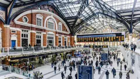 The inside of Liverpool Street station. It has a glass ceiling and a notice board showing the train times. 