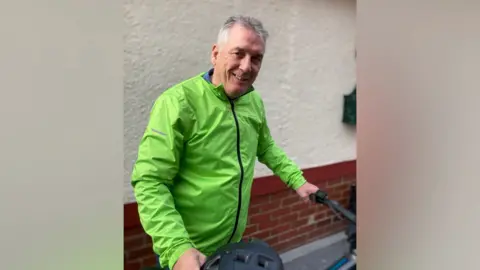 Kevin Hill wore a fluuscent green jacket and caught his bike and a helmet and smiling.