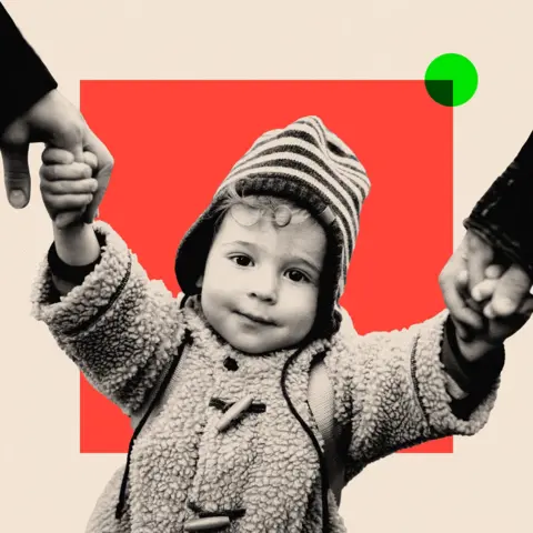 BBC A child wearing a coat and hat, holding hands with their parents