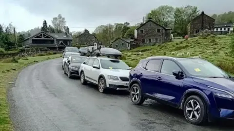 Westmorland and Furness Council A line of cars by the side of an open rural road with yellow parking tickets in front of a number of stone cottages.
