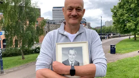 Pam Caulfield/BBC Peter Rowe holds a picture of his father at the D-Day memorial in Castle Park in Bristol