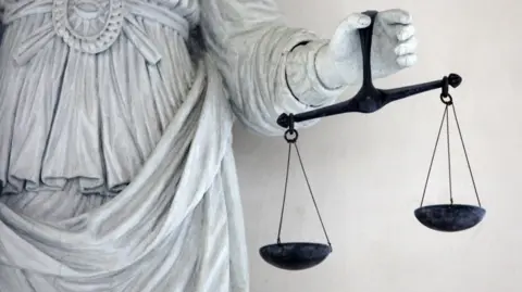 The hand of a grey statue holding black scales of justice