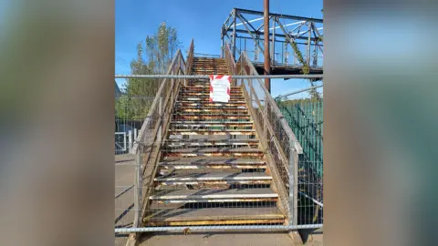 The fenced off pedestrian footbridge at South Bank railway station. There is a red and white sign on the fencing but it is illegible. 