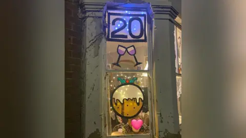 DRARA A festive window decorated as part of the trail during a previous year. It has two clinging glasses and a Christmas pudding. The number 20 is displayed a the top of the window.