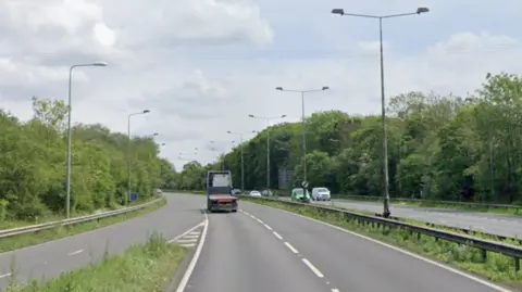 A dual carriageway with a junction joining the road to the left hand side, a lorry up ahead and vehicles on the opposite carriageway 