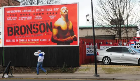 Anna Gowthorpe/PA Archive/PA Images A large poster on a street advertising the movie Bronson, featuring Tom Hardy stripped to the waist against a red backrgound. Visible behind the billboard is the roof of Wakefield Prison.