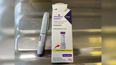 A Mounjaro pen injection device sits next to the carboard packaging.