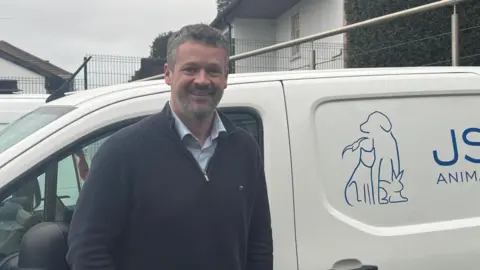 Tom Noel smiling in front of a JSPCA van wearing a navy quarter zip.