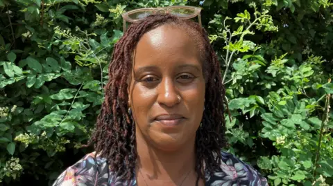 Tanya Obeng in front of green foliage. She wears glasses on her head.