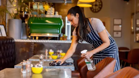 A woman working in a coffee shop cleans a table