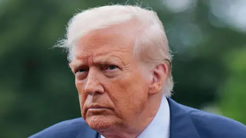 Donald Trump looks into the distance, brows furrowed. He wears a white shirt and blue blazer.