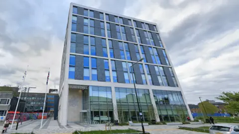 Google The medium-rise town hall building in Crawley on an overcast day. The lower floors of the building are mostly glass-fronted while the upper floors have smaller windows and grey cladding.