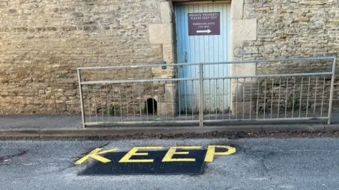 A stretch of road that has recently been patched. The word "Keep" has been written on the patch in yellow lettering. 