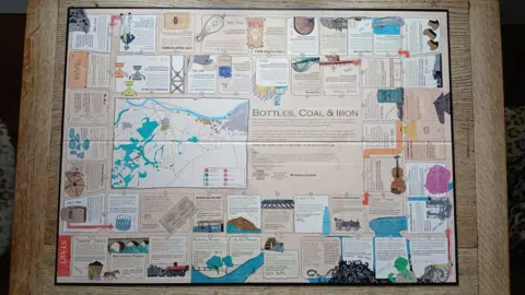 Tyne Derwent Way A view of the board from above. It has "Bottles, Coal and Iron" written near the centre along with a map of the area featured in the game. Dozens of slots around the board feature the names of companies or locations.