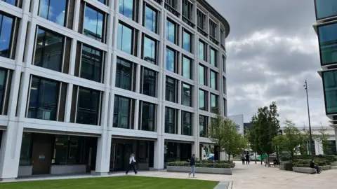 One of Jersey's finance buildings with greenery a walk way and some trees in front with people walking.