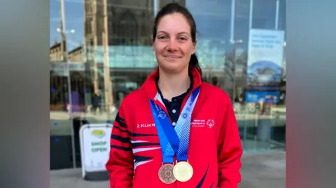 BBC Annabelle Lamb in a red training top, with a gold and bronze medals around her neck on blue and white ribbons