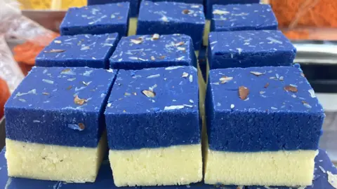A tray of indian sweets called barfi which is a double layer of white on the bottom and blue on the top and they have chopped almonds on top and have been cut into square chunks