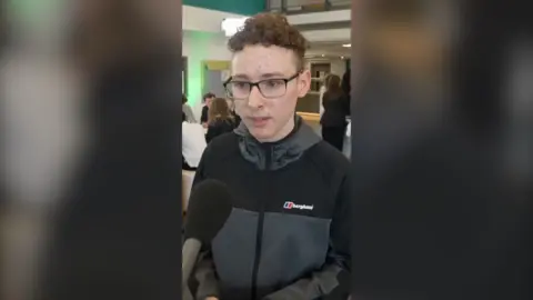 Young person in a zip up coat speaking into a microphone