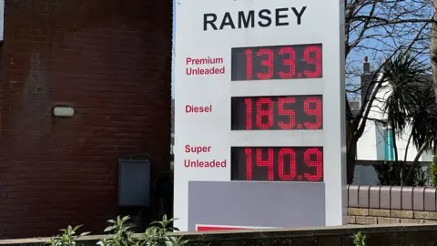A large white sign with the word Ramsey above, detailing the current price of three fuels in large red numbers. It shows premium unleaded at 133.9, diesel at 185.9 and super unleaded at 140.9.