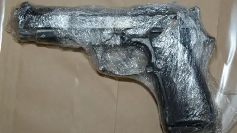 PSNI A black handgun lying on a flat surface, wrapped in clear plastic.