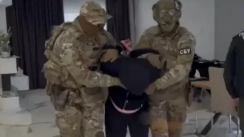 SBU A man in black is taken away by two uniformed men in khaki