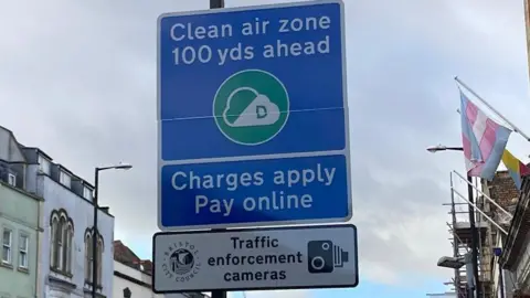 BBC A blue clean air zone sign in Bristol. It says clean air zone 100 yards ahead, charges apply, pay online. 