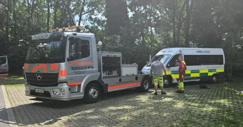 Rotary Club of Northampton Becket Ambulance being towed by grey and orange breakdown truck
