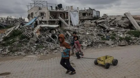 Getty Images Palestinian children pass destroyed buildings and improvised shelters in Beit Lahia, Northern Gaza 