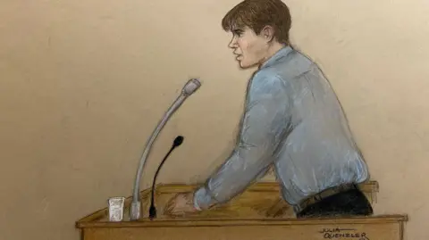 A court room sketch of Johannes Natland. In the hand drawn picture he is wearing a blue shirt and navy trousers as he stands in the dock, resting on one arm. There is a microphone stand and a glass of water in front of him.