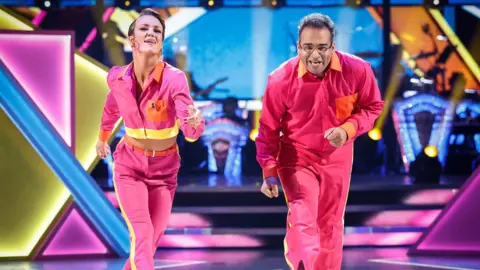 Lauren Oakley and Krishnan Guru-Murthy performing on Strictly Come Dancing 2024 - they are both wearing bright pink tops and trousers with yellow stripes.