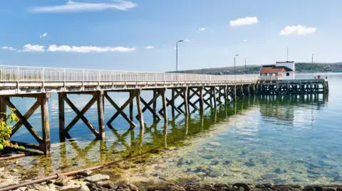 Allen Walley A long pier extending into calm, clear water. 