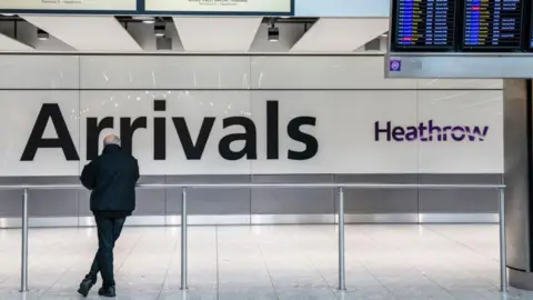 Man waiting in front of a big 'arrival' sign at Getty Images Heathro Airport