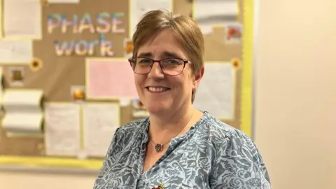 A woman stands in front of a school board full of work. She is smiling at the camera 