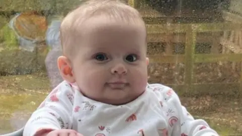 Family handout Penelope Greathead, a baby girl wearing white patterned baby clothes. She is sitting against the backdrop of a rainy window.