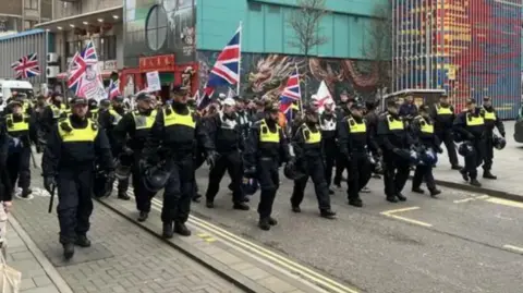 A small group of protesters with British and English flags march with a larger police escort
