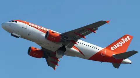 Getty Images A white and orange Easyjet plane in mid-flight against a bright blue sky