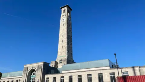 The tower of Southampton City Council stands tall in a clear blue sky. It is made of sandstone and has a big clock at the top. 
