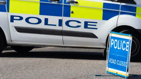 A police van parks next to a "police road closed" sign.