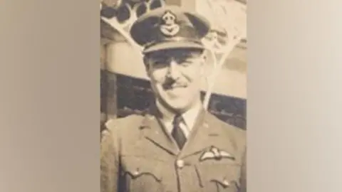 Black and white image of man - Flt Lt James "Cookie" Long - in RAF uniform and cap, smiling at camera.