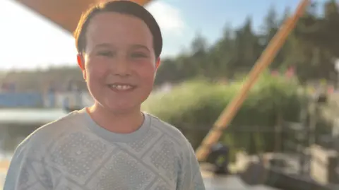 Jon Wright/BBC A boy stands on a stage in the sunshine.