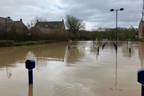 A car park under water. Trolley station rails and bollards can be seen poking out above the water line.