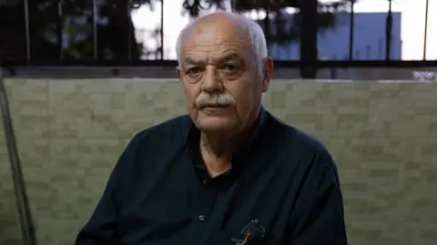 Kasem Abu al-Hija sits in a vigil for his family members. He is a man in his 60s with a grey moustache