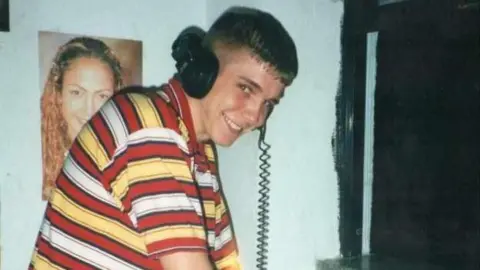 Family A man wearing headphones and a yellow, red and white striped shirt, looks up and smiles.